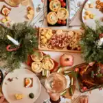Weihnachtlich gedeckter Brunch-Tisch mit Braten, Vorspeisen-Häppchen und Nussschalen zwischen Deko aus Tannenzweigen